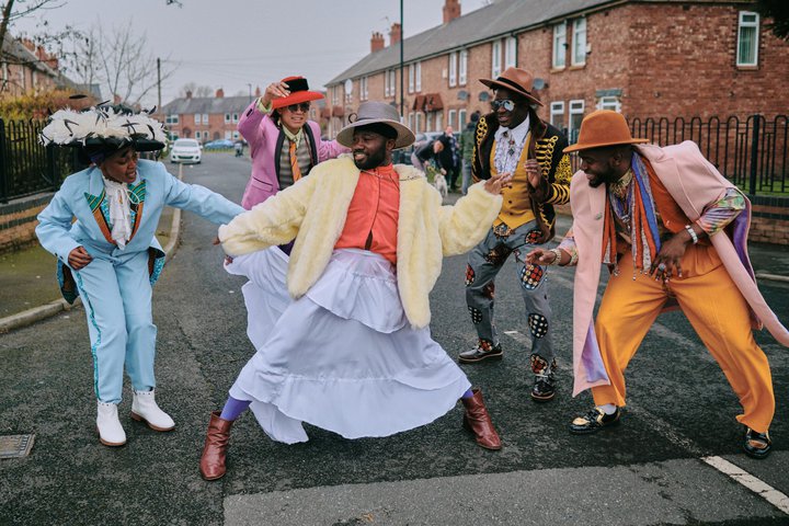 A photograph of five people in a circle dressed in colourful, formal outfits.