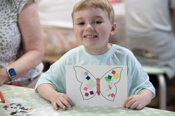 small boy smiles and hold up picture of butterfly