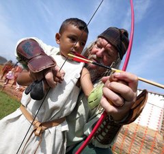 Man helping a young person to learn archery