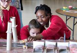 Two young school girls bend over an experiment smiling while a third looks on 