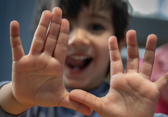Little smiling boy holds up hands to camera