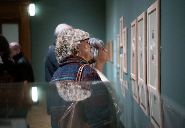 A group of people looking at framed prints on a wall.