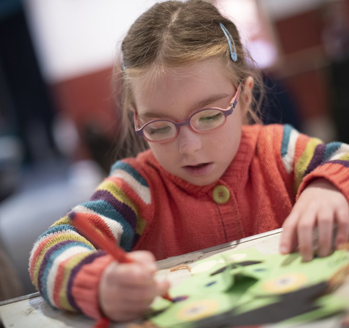 A photograph of a young girl in a striped jumper colouring.