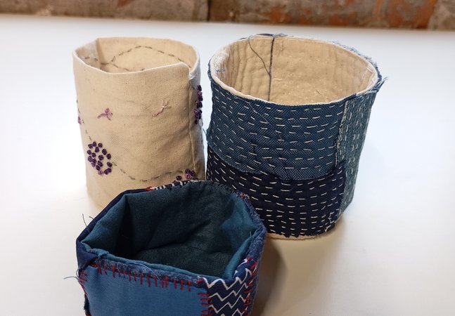 Three hand embroidered fabric round containers in blue and cream
