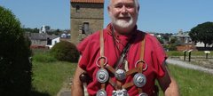 Man in a red tunic, standing with the West Gate in the background