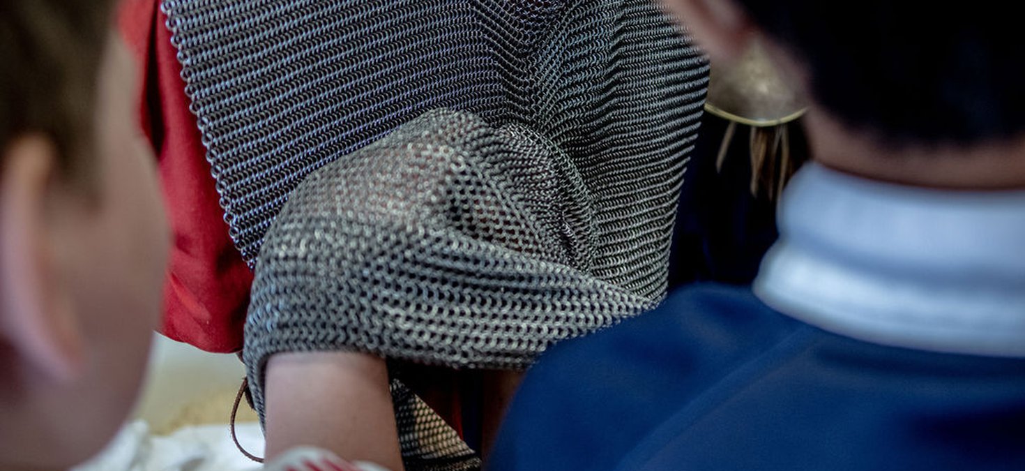 Replica chain mail tunic being worn by a child while two other children inspect the tunic
