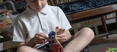 A child is sat on the floor making a proggy mat with craft materials