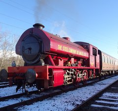 Red steam locomotive pulling passenger carriages on snow covered railway