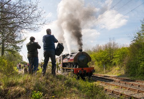 Two people photograph a steam train as it passes by 