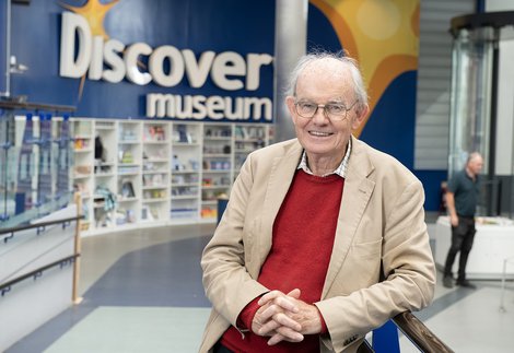 A man smiling and leaning on a railing in front of a sign reading Discovery Museum