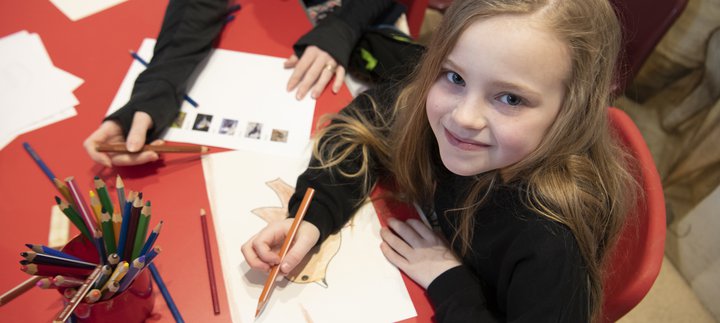 Girl sitting at a red table colouring in some paper