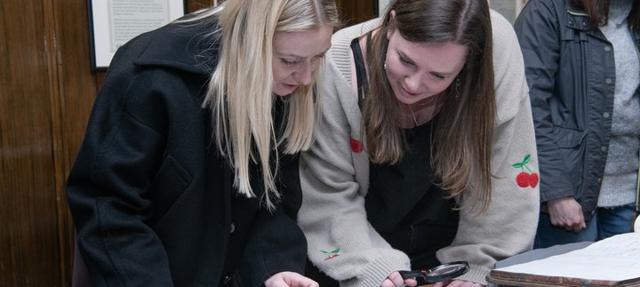 two women bend heads looking at old open book