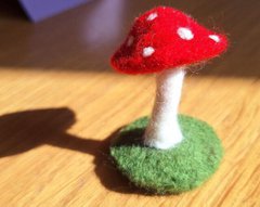 A photograph of a needle felted toadstool. The cap of the mushroom is red with white dots.