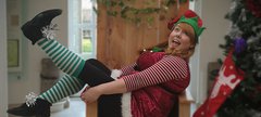 A woman dressed as an elf is sitting on a chair smiling