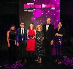 Six people in evening dress receiving an award with a purple screen behind them with the words North East Marketing Awards