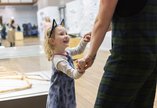 A small child wearing cat ears holds their parent's hand in a museum. She is smiling and laughing
