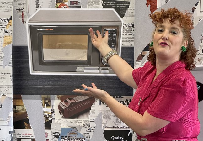A woman gestures extravagantly to an image of a microwave