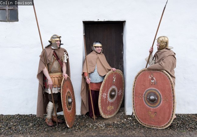 three Roman soldiers stand in front of the reconstructed Barrack Block