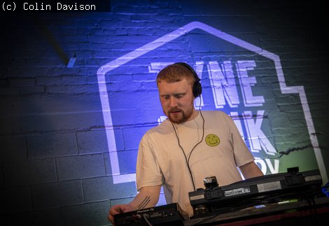 Young man wearing a white t-shirt and headphones DJing at a sound desk. 