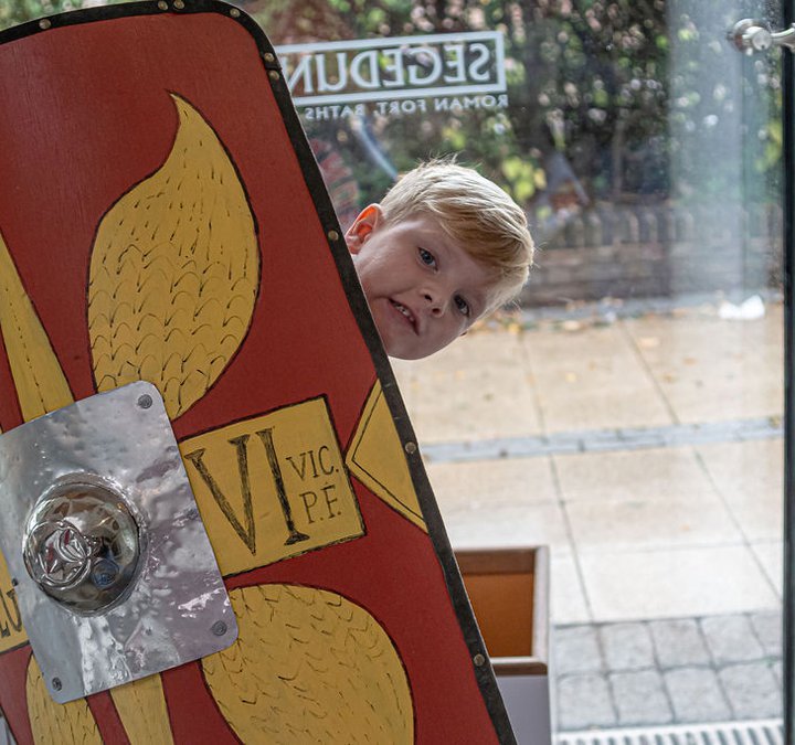 Young boy peeping out from behind a Roman style shield in the shop