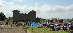 People standing and sitting in front of a Roman style gatehouse on a sunny day