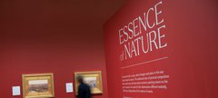 "Photograph of Gallery entrance. Essence of Nature on a red wall with 2 paintings hanging on a wall in the distance