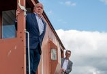 Two men standing looking out of the doorways of a red train carriage