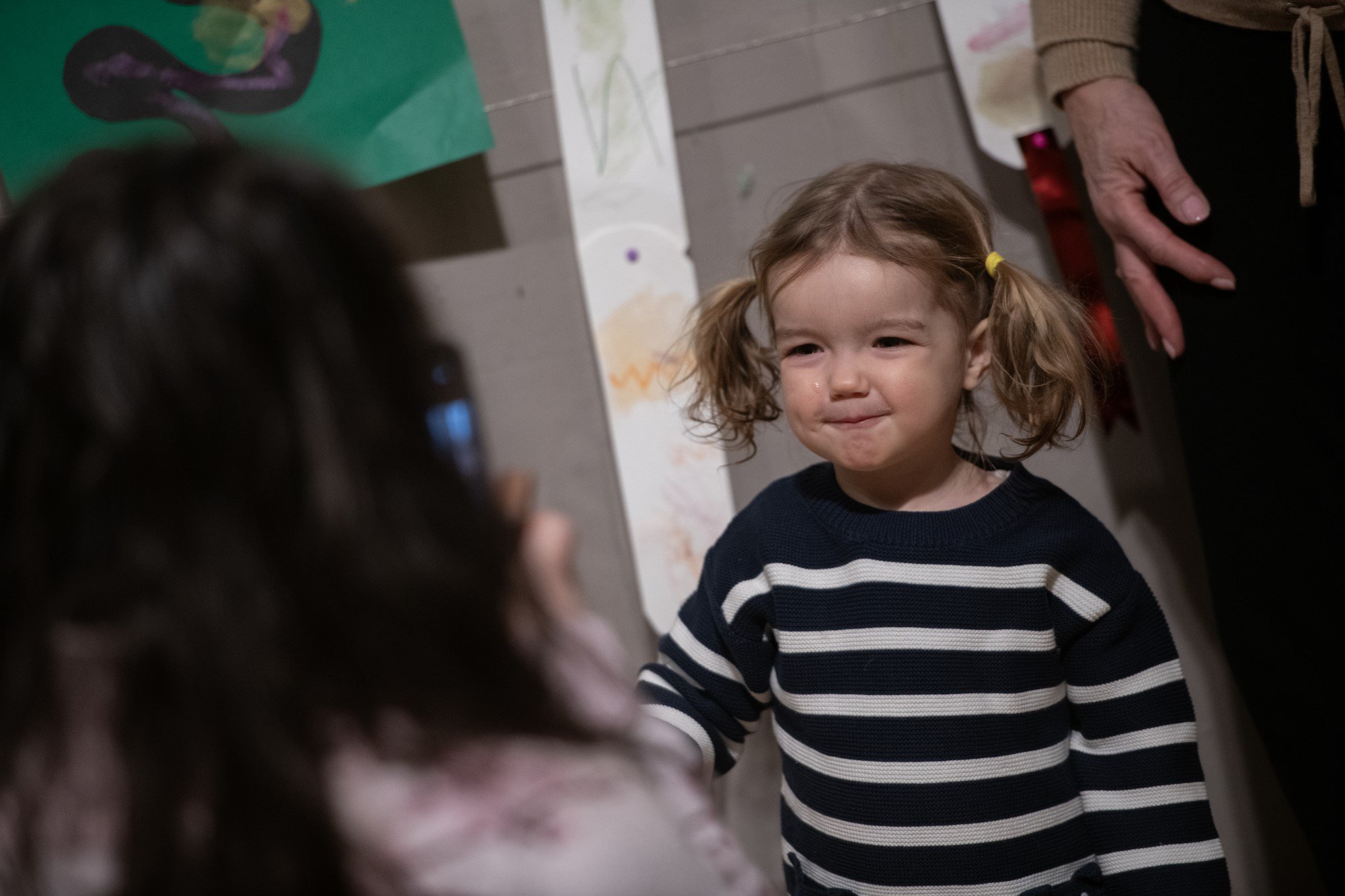 A child wearing a navy and white striped top, smiling at a person behind the camera. A child wearing a navy and white striped top, smiling at a person behind the camera.