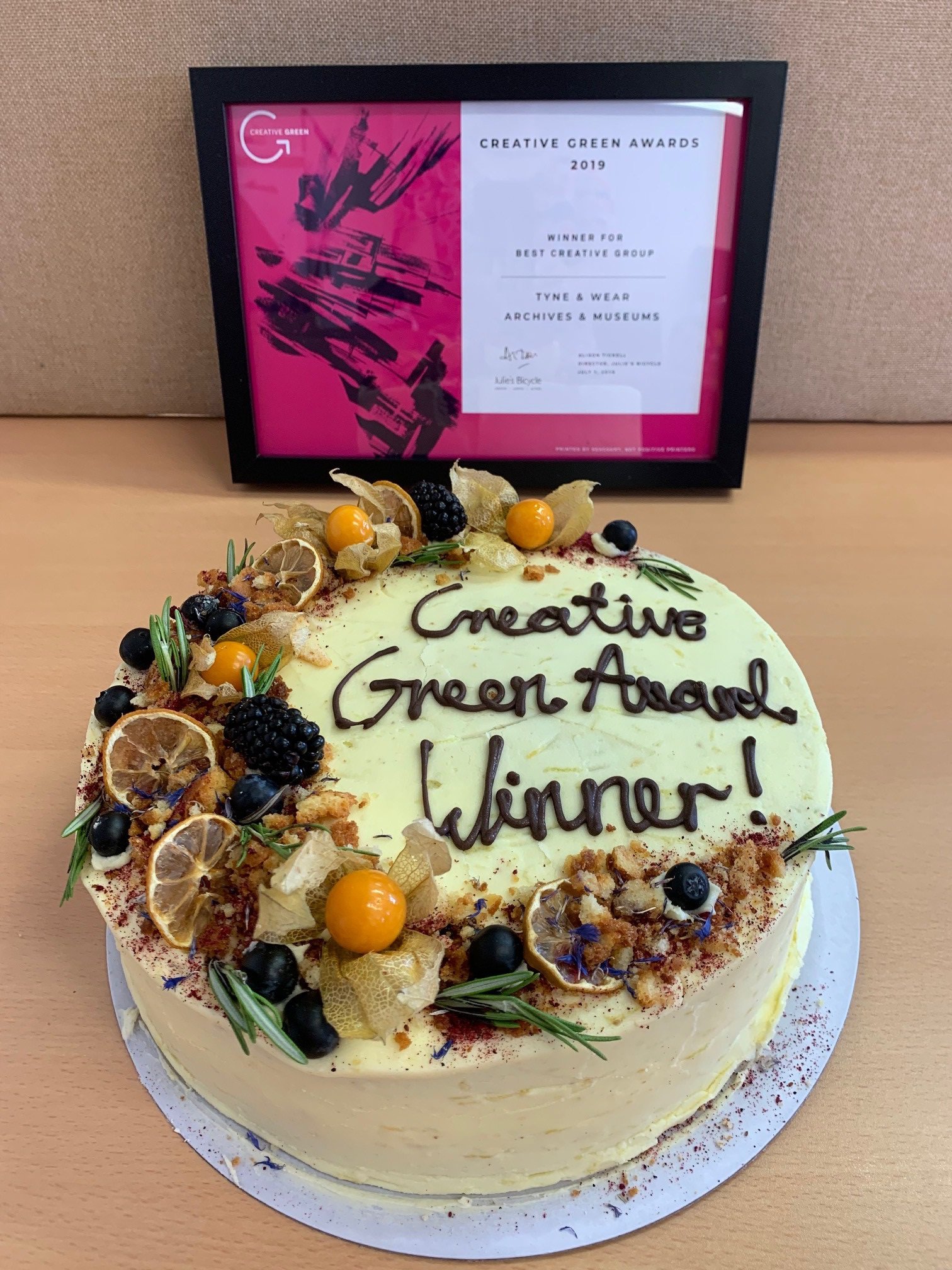 A cake iced with the words Creative Green Award Winner. A certificate to same effect is in the background