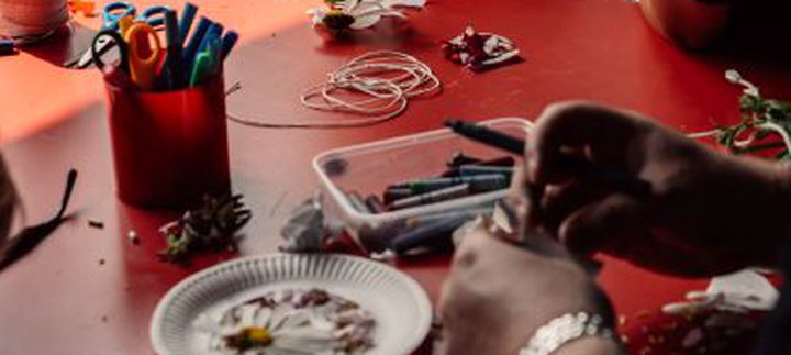 Girl in orange top sat at a craft table with others looking at the craft supplies available