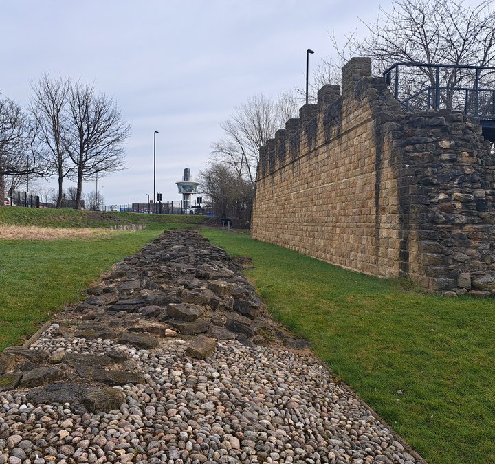 The remains of Hadrian's Wall, with the viewing tower in the distance and a reconstructed section of the wall to the right