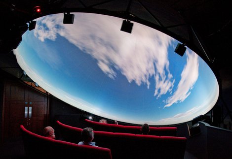Visitors look up at a domed planetarium show. They are seeing clouds moving across a daylight sky