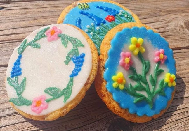 A photograph of three cookies decorated with floral designs. The flowers are pink, yellow, and blue with green stems.