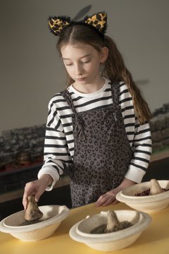 Young girl with long hair and headband and striped long sleeved top grinding herbs with a pestle and mortar