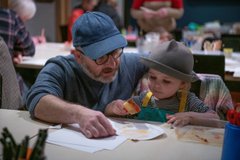 A photograph of a dad helping his young daughter with her arts and crafts.