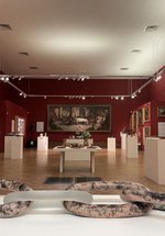 A display of glass and ceramic objects on white plinths in a gallery space.