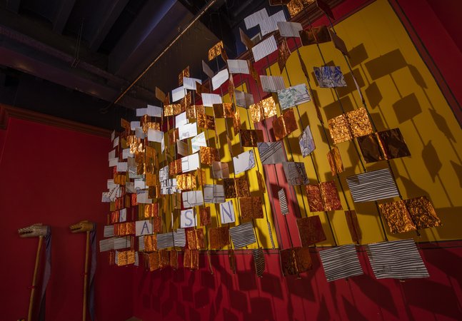 Art installation featuring hanging gold squares and drawings