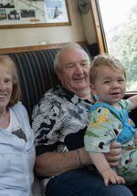 A family of three sit in a train carriage. They are smiling at the camera