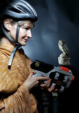 Photograph of a female in a cycle helmet holding a nerf gun with a stone statue of owl in the background