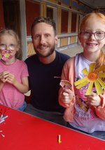 Two young girls with their dad holding the flowers they've made from egg boxes