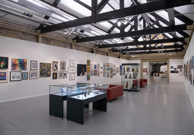 A gallery space with artworks on the walls and glass display cases filled with pottery and sculpture