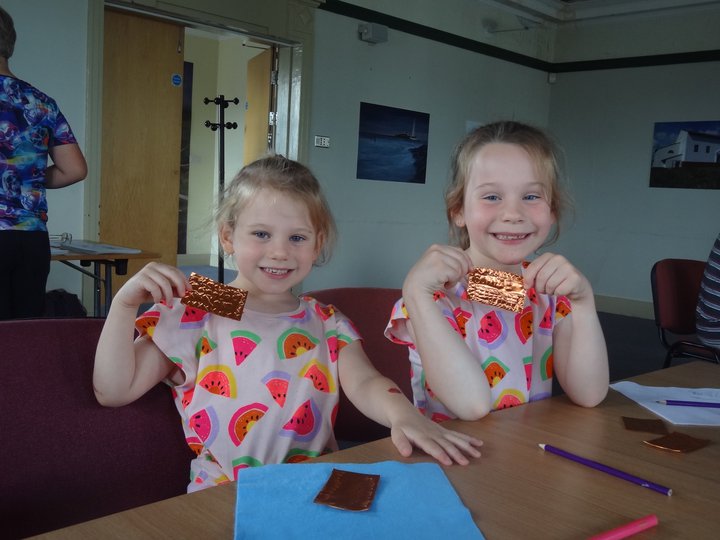 Two young girls holding up the objects they've made