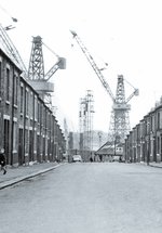 Black and white photo of street with terraced housing leading to shipbuilding yard and cranes