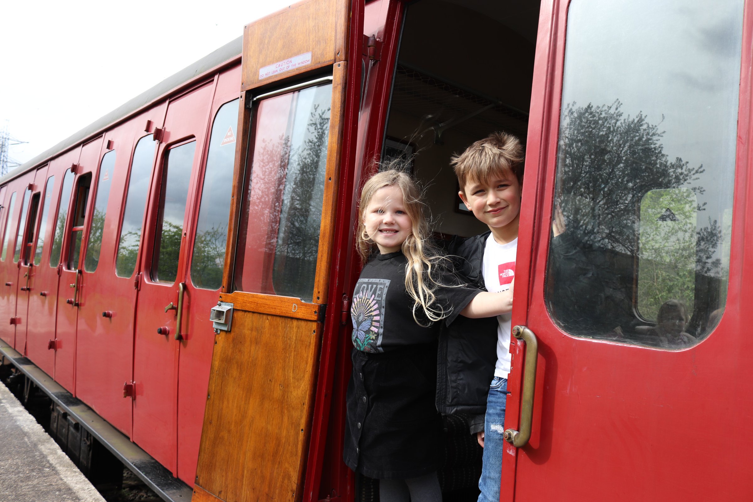 Two children stand at the door of a rail carriage, they are looking towards the camera and smiling. Two children stand at the door of a rail carriage, they are looking towards the camera and smiling.