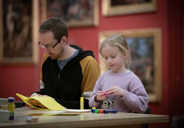 An adult and child sat a table with craft materials.