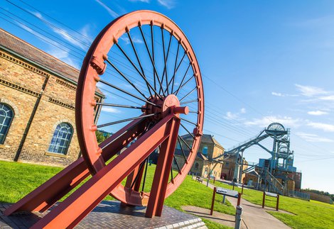 A large metal wheel with a bigger metal structure and wheel in the background