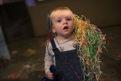 A toddler is covered in shredded coloured paper.