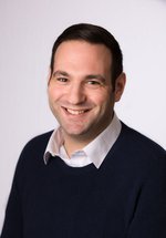 smiling brown haired man in dark jumper & white shirt 