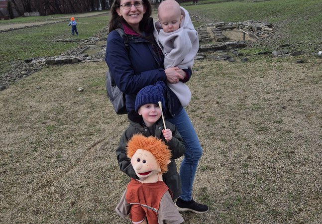 A woman holding a baby while a young child holds a soft toy on the fort site