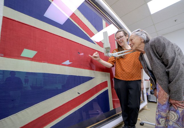 Two women, on older bend and examine a Union flag